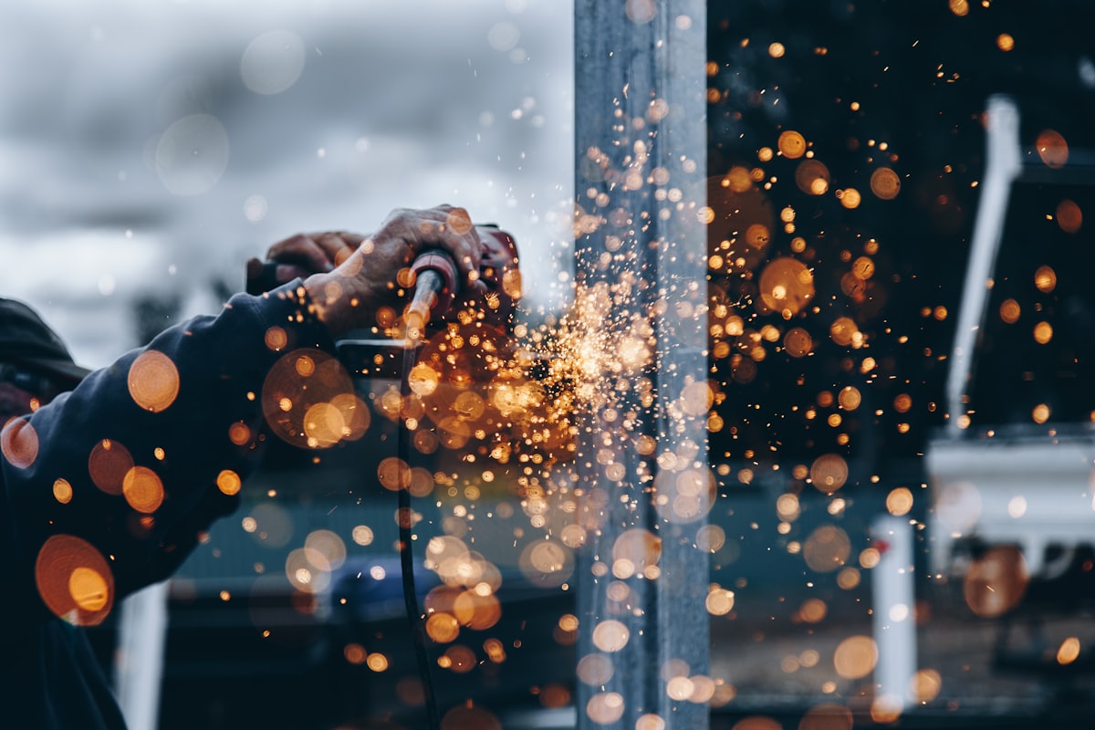 A worker cutting steel with an angle grinder, sparks across the frame
