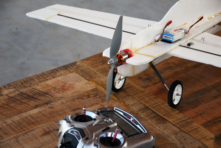 Hand-built white foam model aeroplane with a propeller and battery beside its radio transmitter on a timber table